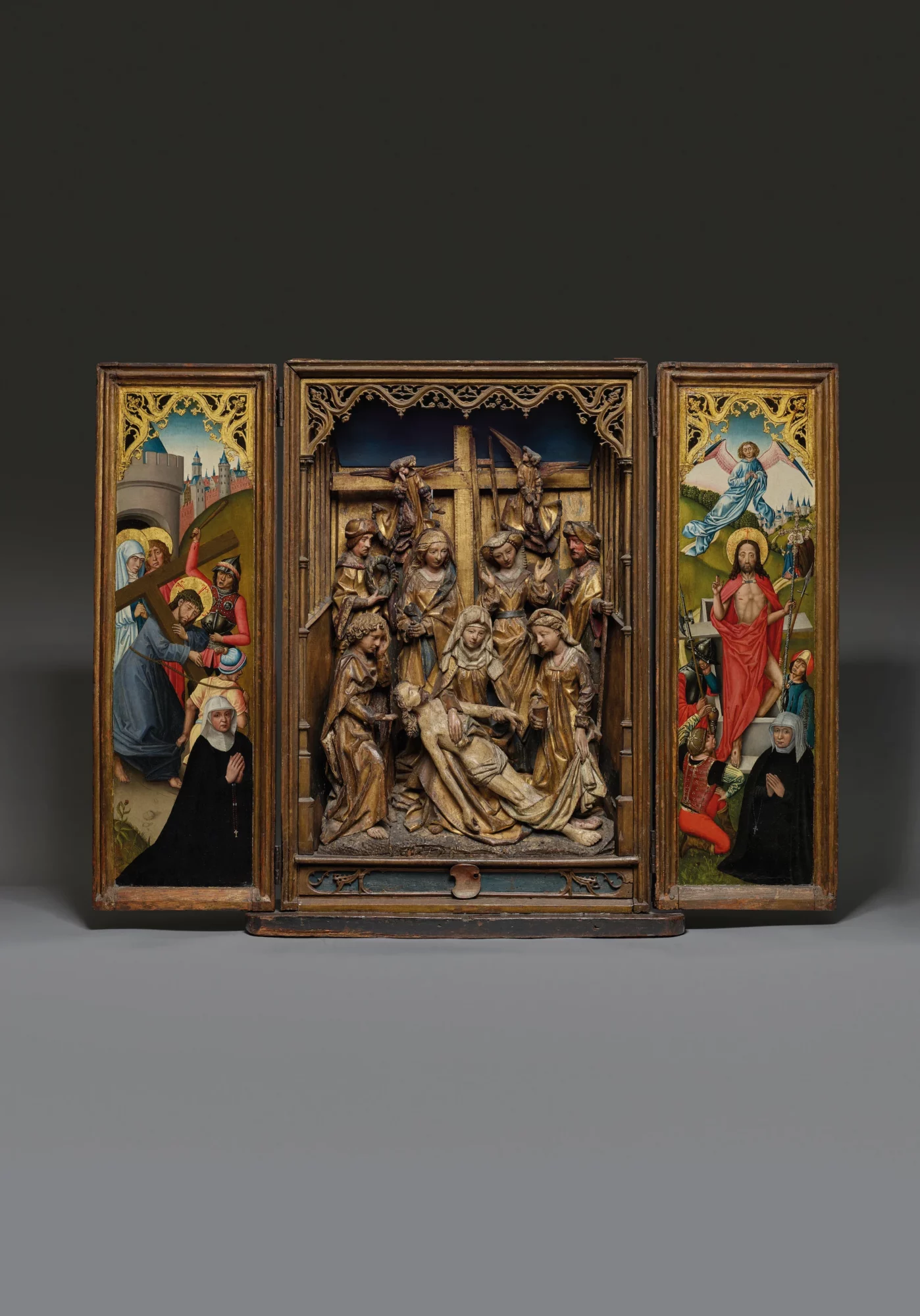 Late Gothic altarpiece with a central sculpted Lamentation of Christ, surrounded by figures supporting and mourning his body. The painted side panels depict the Carrying of the Cross on the left and the Resurrection on the right, each accompanied by kneeling donor figures below.