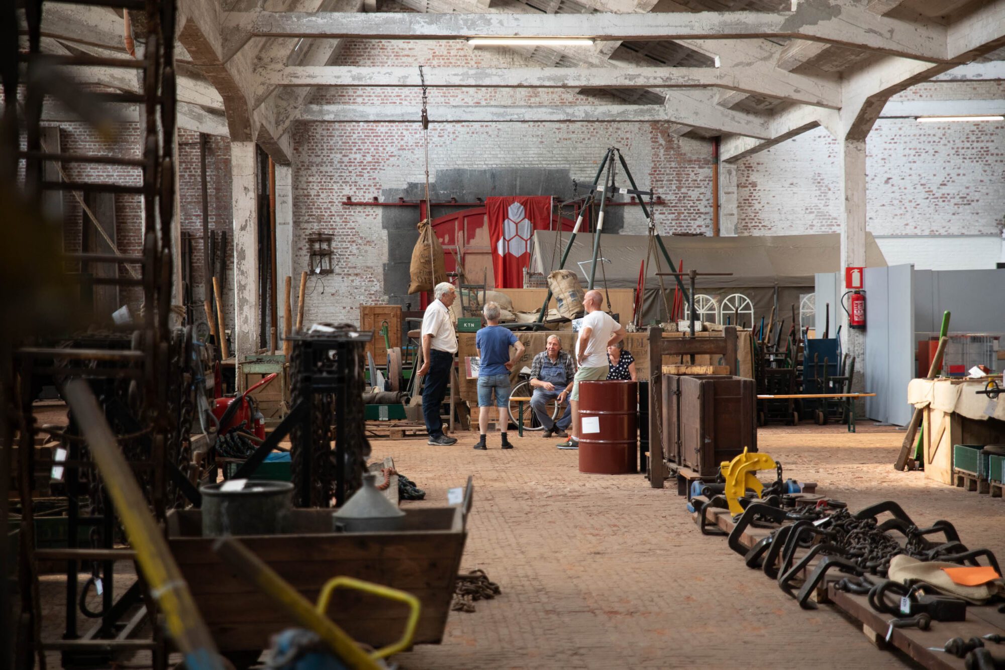 Visitors exploring logistics and maritime heritage in a large historic warehouse with old machinery and port equipment in Antwerp.