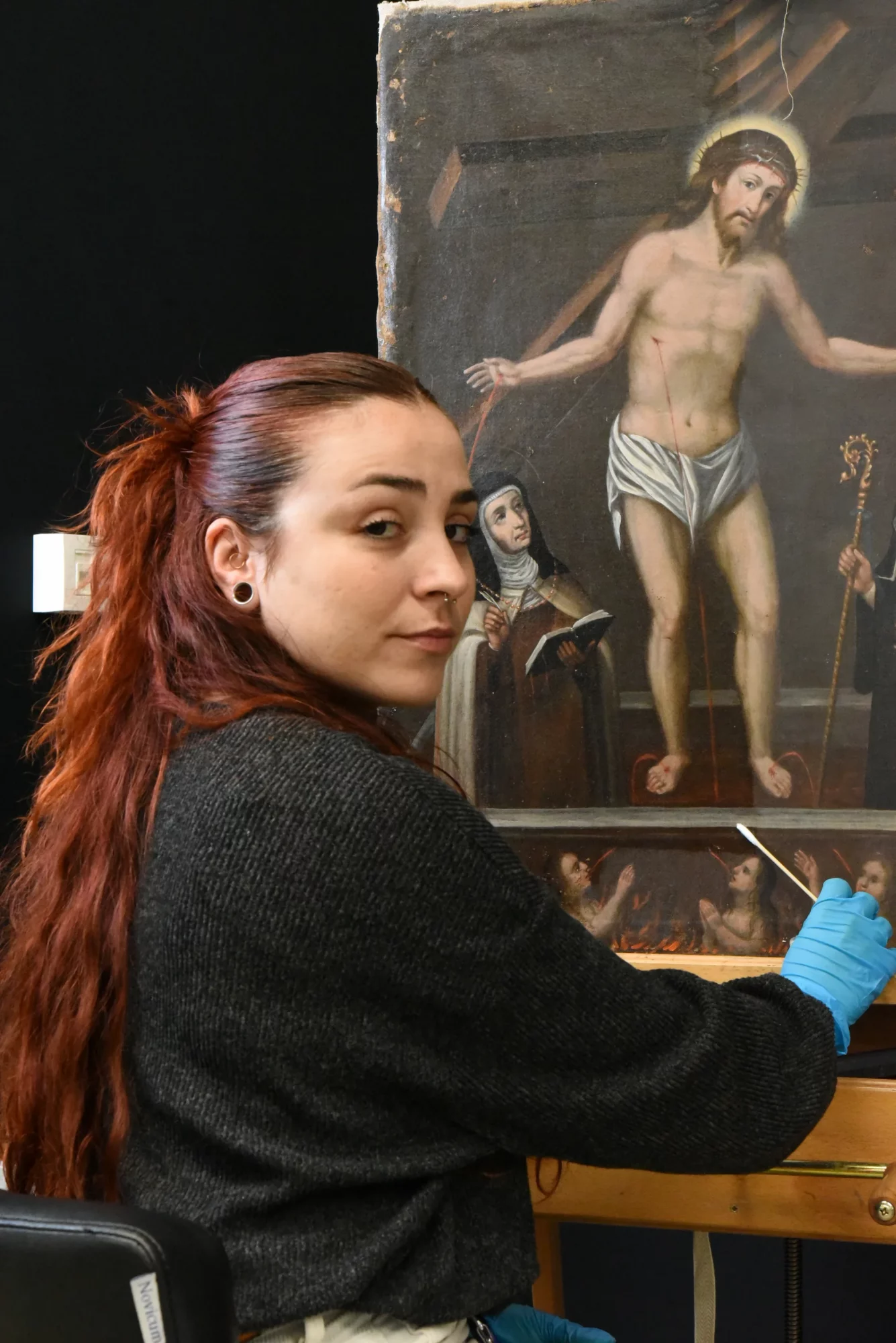 Conservator-restaurator werkt aan de restauratie van een 17de-eeuws schilderij waarop de verrezen Christus en de heiligen Gertrudis en Teresa zijn afgebeeld.