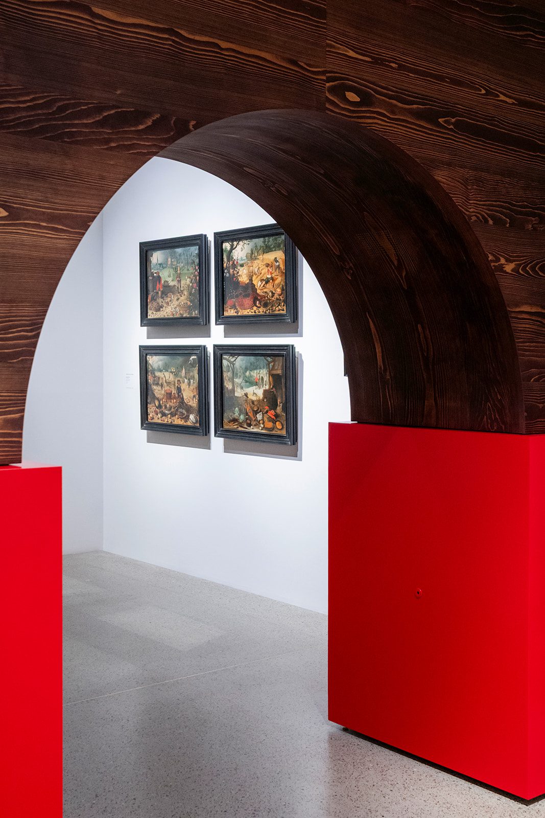 Four seventeenth-century paintings displayed beneath a monumental wooden arch in the scenography of Garden of Delights at Museum De Lakenhal.