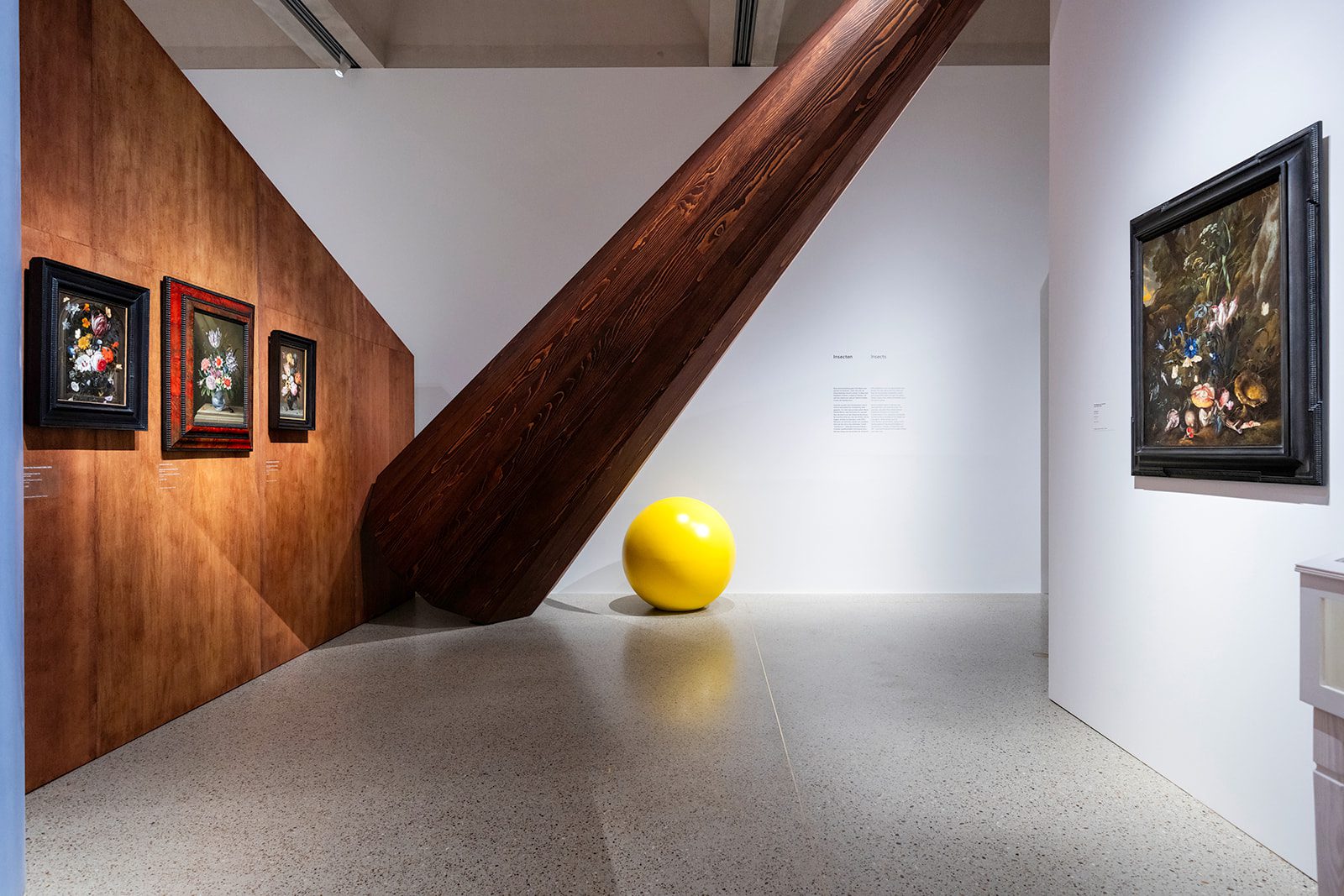 Seventeenth-century flower still lifes in Garden of Delights, displayed against wooden walls and a monumental beam with a striking yellow sphere.